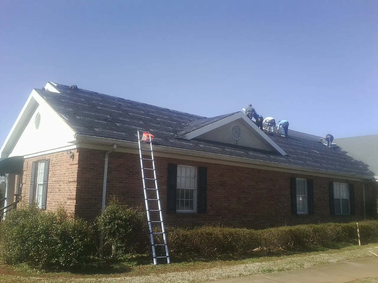 Crew tearing shingles off a brick ranch roof with a ladder set — Metal Roof Repair work by our crew in Karns City