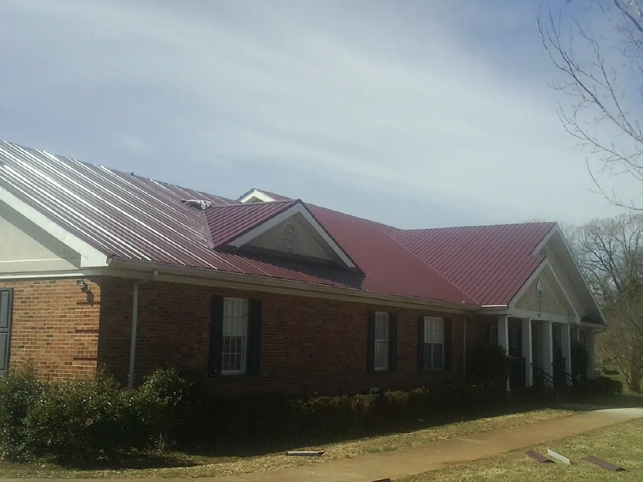 Red metal roof with gabled entries on a long brick building, from a Hail Damage Roof Repair job in Karns City