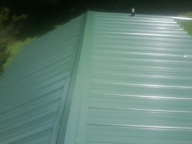New green metal panels meeting at the ridge of a roof — Flat Roof Repair work by our crew in Karns City