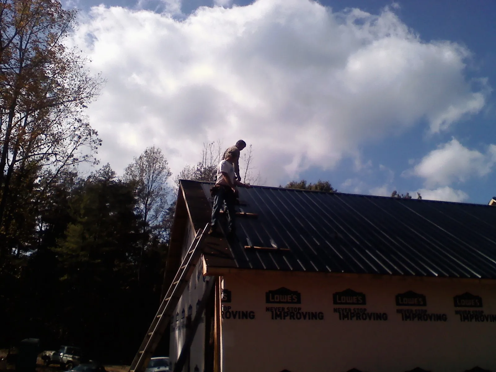 Roofer fastening dark metal panels high against a cloudy sky, from a Roof Inspection job in Karns City