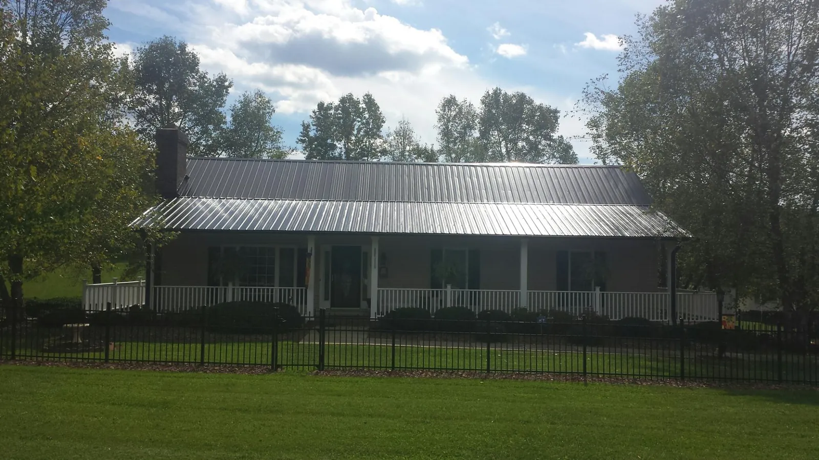 Gray metal roof on a brick ranch with a full width front porch — Gutter Guard Installation work by our crew in Karns City