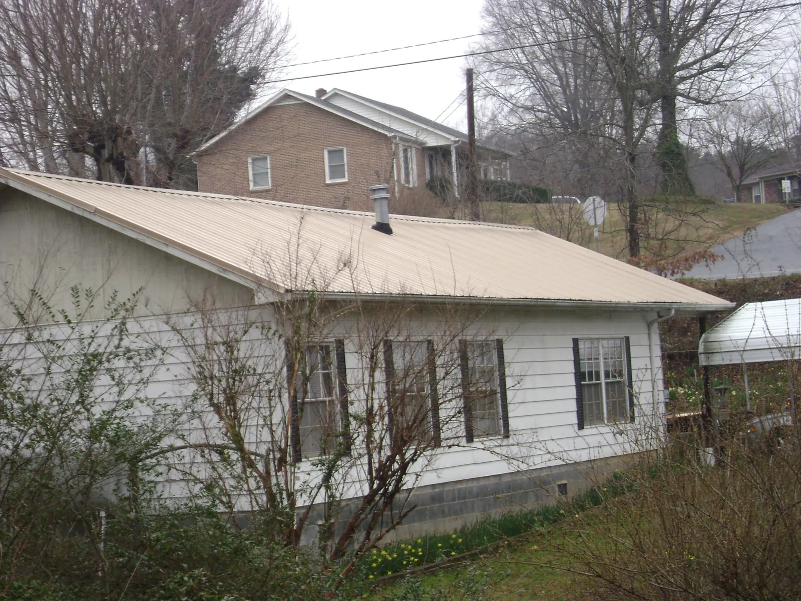 Tan metal roof on a white sided house set into a hillside — Commercial Roofing by Roofing Brothers in Karns City